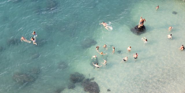 This image depicts an aerial view of people swimming and enjoying clear blue ocean waters. Ideal for travel websites, brochures promoting beach vacations, and summer-related marketing materials.