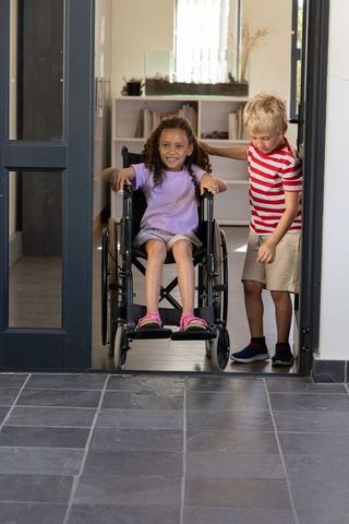 Smiling girl in wheelchair with boy guiding through doorway, childhood accessibility