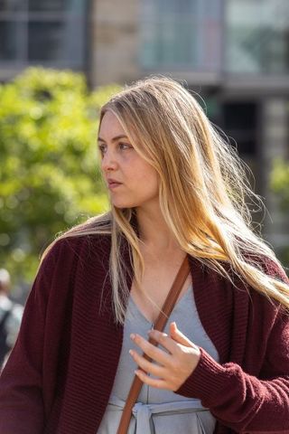 Walking woman wearing burgundy knit and gray dress with crossbody strap looking in urban plaza