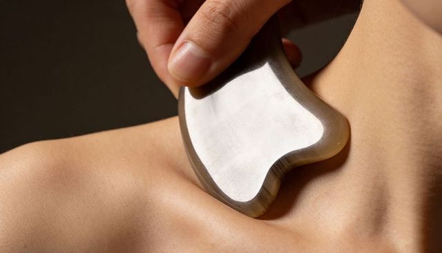 Practitioner massaging neck and shoulder with gua sha stone for wellness and relief