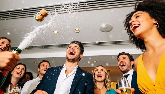 Group celebrating with champagne spray, laughing guests at party reception