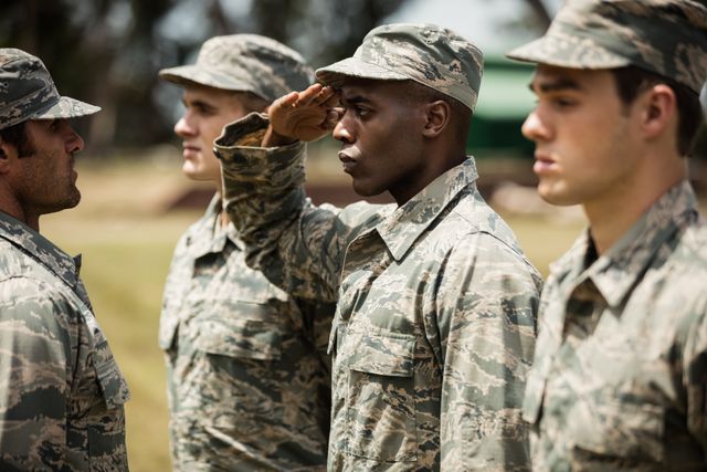 Group of soldiers receiving training from a military trainer at a boot camp. One soldier is saluting while others stand in formation. Useful for illustrating military training, discipline, teamwork, and leadership in armed forces.