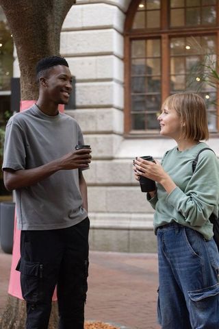 Friends chatting while holding takeaway coffee on city sidewalk with arched windows