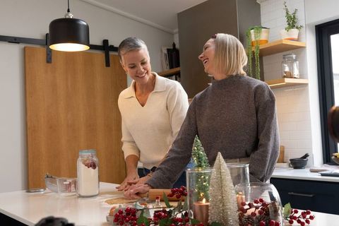 Mature women baking cookies together in cozy modern kitchen with holiday decorations and laughter