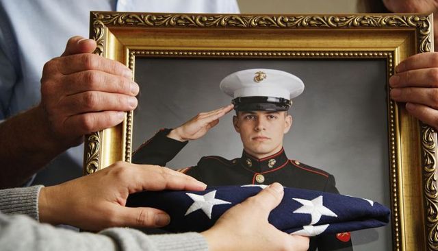 Family holding framed portrait of saluting marine while displaying folded american flag