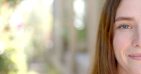 Young woman smiling in sunlit garden corridor with flowering shrubs