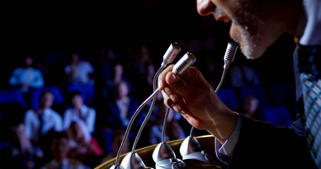 Speaker is addressing an audience at a conference through multiple microphones. The audience is blurred for focus on the speaker. This can be used in articles or materials related to public speaking, business presentations, conferences, leadership, and communication skills.