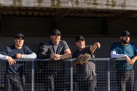 Amateur baseball team leaning on dugout railing, watching game and pointing toward field
