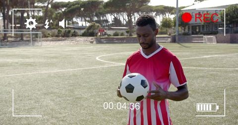 Male soccer player holding ball on artificial turf being filmed with rec overlay