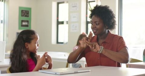 African american teacher teaching sign language to young student in bright classroom