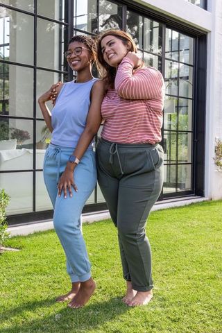 Friends standing barefoot on lawn in joggers smiling by modern glass house windows