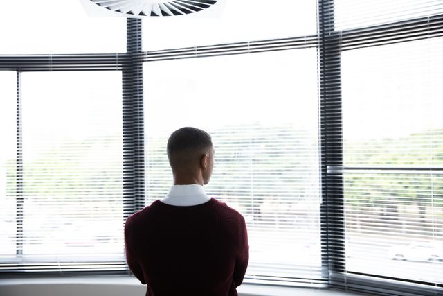 Rear view of a young African American man with short dark hair looking thru the window in the office of a creative business.