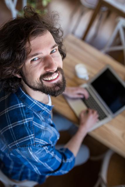 Portrait of smiling man looking up while using laptop in coffee shop