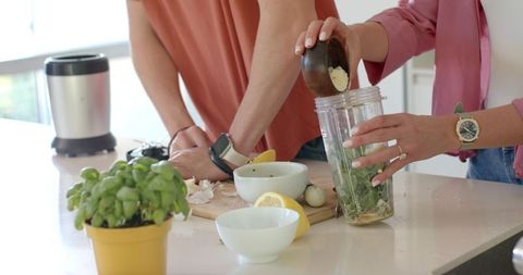 Couple preparing fresh herb pesto and green smoothie in bright modern kitchen