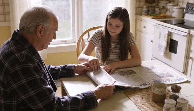 Grandfather and granddaughter sharing morning newspaper at cozy kitchen table bonding