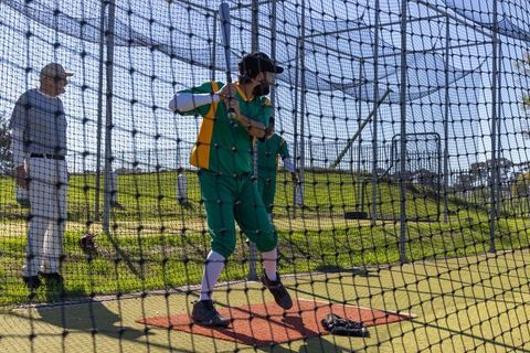 Batter practicing swing in batting cage while coach signaling during baseball training
