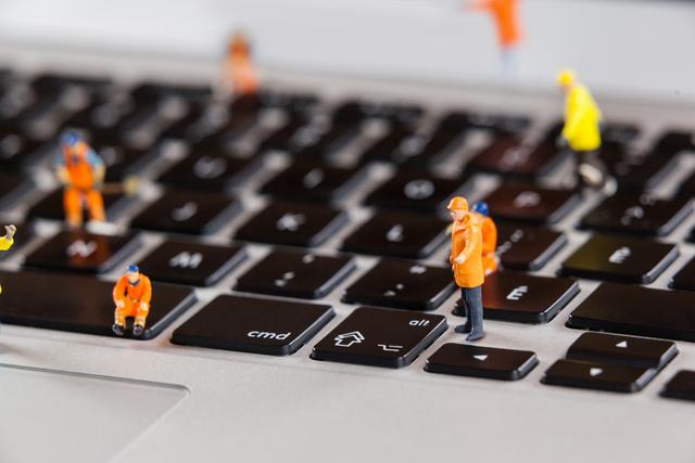 This image shows miniature workers in orange uniforms repairing a laptop keyboard. Ideal for illustrating concepts of technology maintenance, IT support, teamwork, and computer repair. Suitable for use in blogs, articles, presentations, and marketing materials related to technology, IT services, and hardware maintenance.