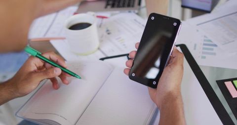 Person Using Smartphone and Writing in Notebook at Home Office