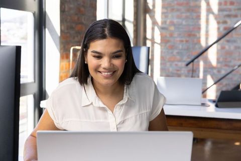 Smiling Woman Working on Laptop in Industrial Office