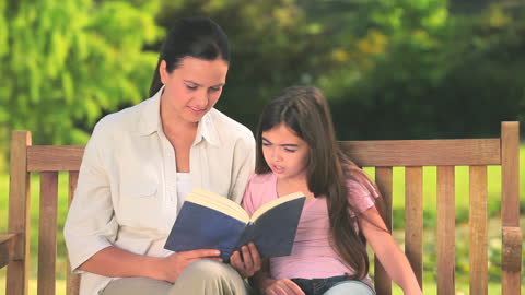 Mother and Daughter Bonding Over Book on Sunny Park Bench