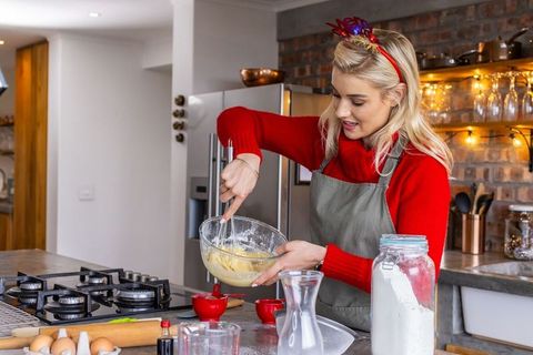 Young woman mixing cake batter in cozy rustic kitchen wearing red sweater and apron