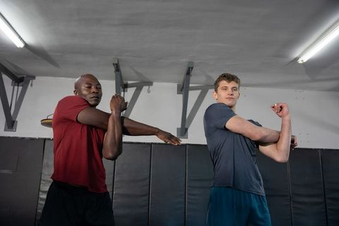 Partner-assisted arm stretch for athletes practicing martial arts in dojo with padded walls