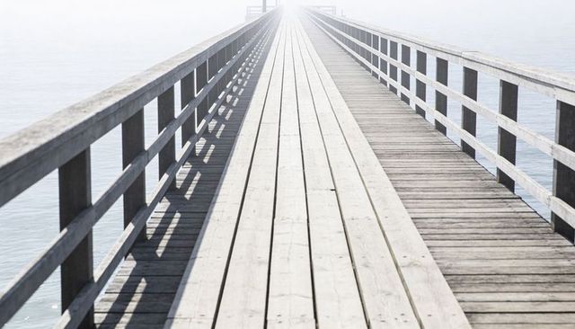 Wooden pier vanishing into misty horizon over calm sea with strong perspective lines