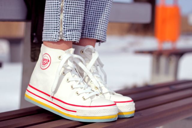 Woman sitting outdoors wearing stylish white sneakers with colorful soles. Ideal for use in fashion blogs, casual lifestyle promotions, sneaker ads, trendy footwear catalogues, and outdoor activity promotions.