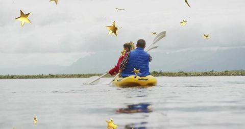 Couple paddling yellow kayak surrounded by golden stars