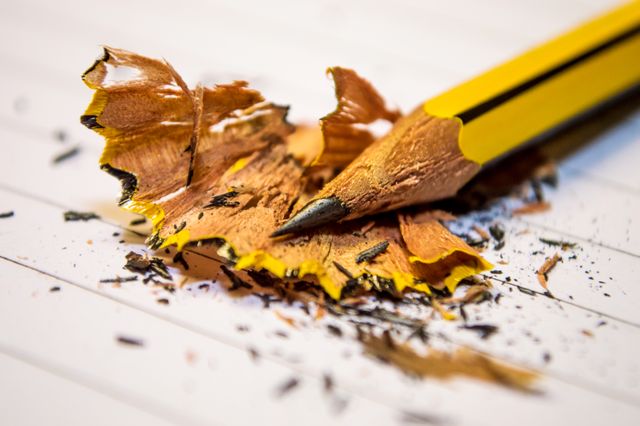Detailed close-up of a sharpened yellow pencil surrounded by wood shavings on lined paper. Ideal for illustrating themes of creativity, education, writing, study habits, office supplies, and crafting projects.