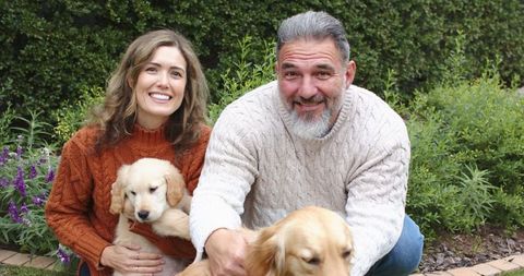 Couple in knit sweaters smiling, holding golden retriever puppy and petting retriever