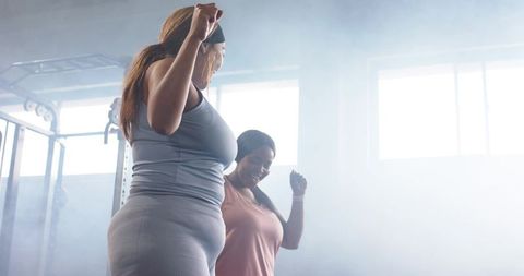 Diverse plus-size women warming up and stretching together in gym near power rack
