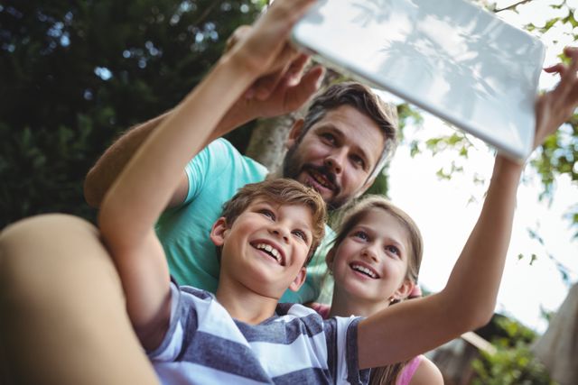 Father and kids taking a selfie in garden with digital tablet