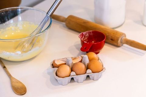 Home baking prep showing egg carton, whisking bowl, wooden spoon and rolling pin on bright counterto