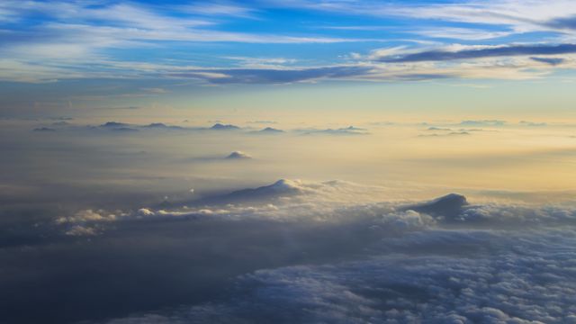 Shot captures tranquil, misty mountain peaks at sunrise from an aerial perspective, above the clouds. Ideal for travel blogs, meditation themes, and nature enthusiasts. Suitable for wall art and inspirational visuals.
