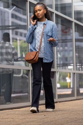 African woman talking on smartphone and gesturing while walking past glass facade