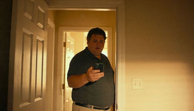 Man checking smartphone in warm home hallway holding phone, casual polo and khaki pants