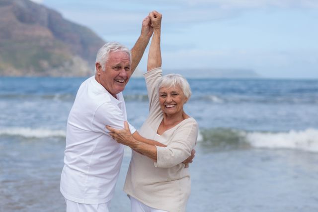 Senior couple enjoying a day at the beach, smiling and having fun. Perfect for themes related to retirement, healthy living, active seniors, and vacation. Ideal for use in advertisements, brochures, and websites promoting senior lifestyle, travel, and wellness.