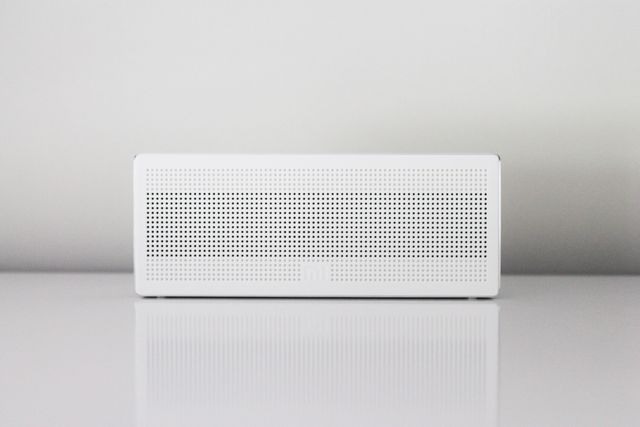 Minimalist Bluetooth speaker on white surface provides a clean and modern look, ideal for use in tech blogs, product reviews, e-commerce websites, and promotional materials for audio equipment. The simplicity adds a contemporary aesthetic, making it versatile for various digital media needing a modern and sleek touch.