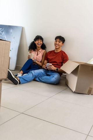 African american asian couple relaxing with mugs amid moving boxes in modern minimal home