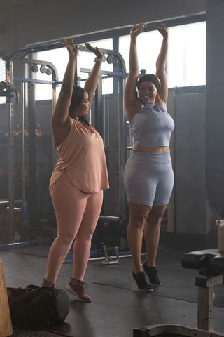 Two african american women stretching together in gym showing body positive fitness
