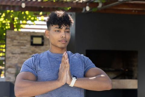 African american man practicing prayer on backyard patio under pergola, wearing smartwatch