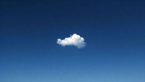 Solitary cumulus cloud drifting across deep blue sky with soft gray underside