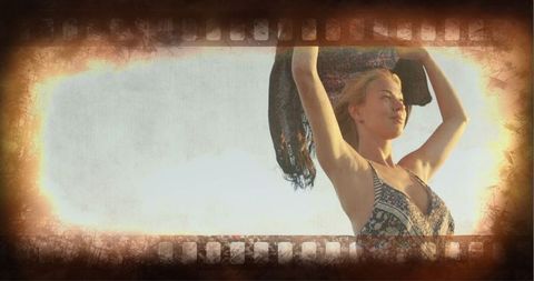 Carefree woman holding shawl on beach at sunset