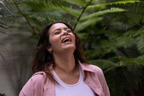 Laughing young woman enjoying lush garden greenery wearing pink shirt and hoop earrings