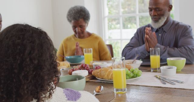 Image of happy african american parents, daughter and grandparents saying grace at dinner table. Family, domestic life and togetherness concept digitally generated image.