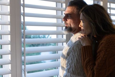 Couple standing and gazing through white shutters wearing cozy cable knit sweaters