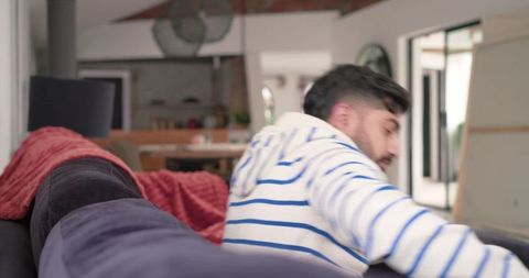 Indian man reaching on sofa in modern open-plan living room with friend sitting nearby
