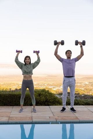 Diverse couple exercising with dumbbells outdoors by pool