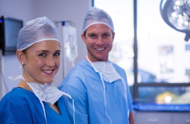 Male and female nurses wearing surgical attire, including scrubs, caps, and masks, smiling in an operation theater. Ideal for use in healthcare promotions, medical advertisements, hospital websites, and educational materials about medical professions.